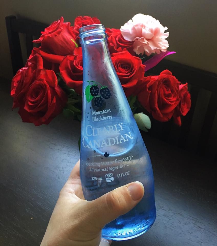 Clearly Canadian Mountain Blackberry Bottle 325ml Partially Empty in Front of Roses
